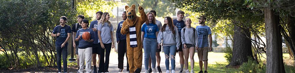 students walking on pathway through the woods with the Nittany Lion mascot